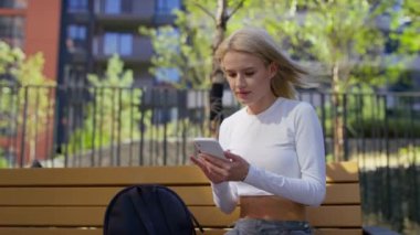 Genç bir kadın dışarıda otururken akıllı telefonuna bakarken şaşkınlıkla tepki veriyor..