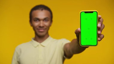 Elinde yeşil ekranlı akıllı bir telefon tutan genç adam, parlak sarı bir arka plana karşı, taklit amaçlar için mükemmel..