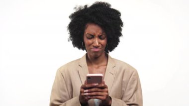 Telefonuna kaşlarını çatan kıvırcık saçlı kadın beyaz arka plana karşı hoşnutsuzluk ya da kafa karışıklığı ifade ediyor..