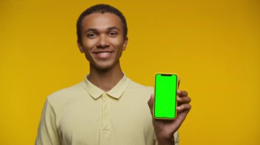 Mutlu genç adam yeşil ekranlı akıllı telefonu canlı sarı bir arka plana gösteriyor, model için hazır..