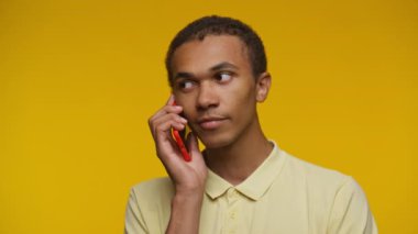 Kırmızı akıllı telefonu kulağına dayamış gülümseyen genç bir adam sarı arka planda sohbet etmekten zevk alıyor..