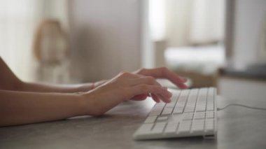 Parlak ve modern kapalı bir ortamda beyaz bir klavyeye yazı yazan ellerin yakın plan görüntüsü, ofis veya uzak çalışma temaları için ideal.