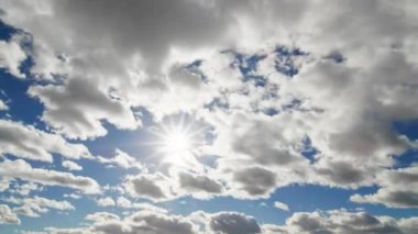 Pofuduk bulutların arasından süzülen, dinamik doğal güzelliği gösteren parlak güneş ışığıyla güneşli bir gökyüzünün hızlandırılmış görüntüsü..