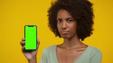 Elinde yeşil ekranlı, sarı arka planlı akıllı telefon tutan şüpheli bir yüzü olan bir kadın..