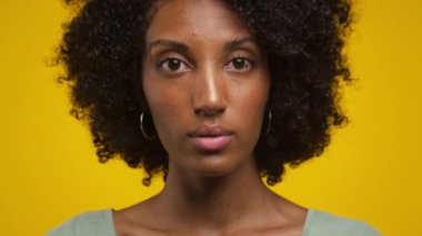 Sarı arka planda halka küpe takan, doğal kıvırcık saçlı bir kadının yakın plan fotoğrafı..