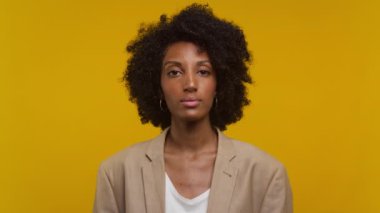 Kendine güveni tam bir kadın portresi bej ceketli ve beyaz bluzlu, canlı sarı bir arka planda duruyor..