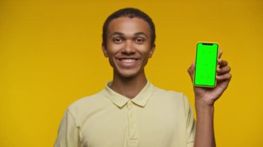 Neşeli bir adam elinde yeşil ekranlı akıllı bir telefon tutuyor, canlı sarı bir arka plana hevesle bakıyor..