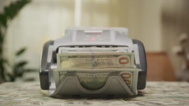 Para sayma makinesinin 100 dolarlık banknotları nakit dolu bir masada sayarken çekilen yakın çekim..