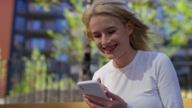 Modern bir şehir ortamında akıllı telefonunu kullanarak diş teli takan mutlu genç bir kadın..