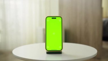 Minimalist, iyi ışıklandırılmış bir iç mekanda şarj standına yerleştirilmiş yeşil bir ekranı gösteren akıllı telefon..