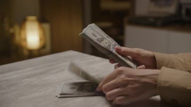 Masadaki 100 dolarlık banknotları sayan eller zenginliği, finansal planlamayı ve refahı simgeliyor..