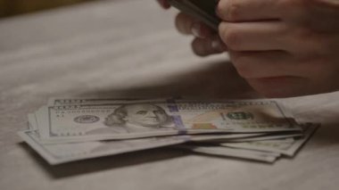 Masadaki 100 dolarlık banknotları sayarak, zenginlik ve mali faaliyetleri temsil eden ellerin yakın görüntüsü.