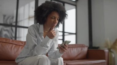 Deri koltukta oturan iş kadını, çağdaş ofis ortamında akıllı telefonunu incelikle analiz ediyor..