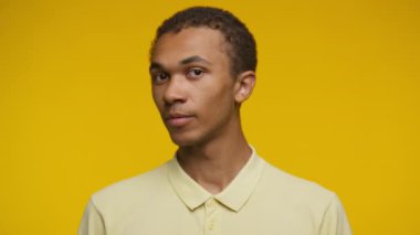 Sarı polo tişörtlü genç bir adam portresi, kendinden emin bir şekilde gülümsüyor ve parlak sarı bir arka plana pozitif yansıyor.