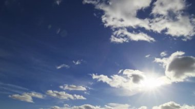 Güneşin zamanı parlak beyaz kabarık bulutların parlak mavi gökyüzünde sürüklenmesi gibi, dinamik havayı yakalıyor.
