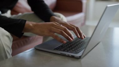 Sıradan bir ortamda otururken dizüstü bilgisayarda yazı yazan ellerin detaylı görünümü.