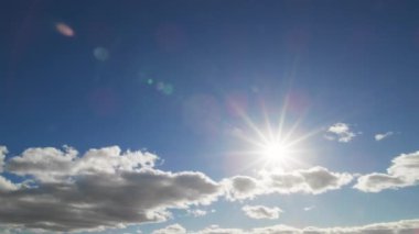 Güneşin, bulutların parlak bir şekilde mavi gökyüzünde sürüklendiği zaman dilimi sahnesi..