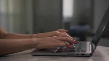 Kapalı bir ortamda dizüstü bilgisayarın klavyesine yazı yazan ellerin yan görünümü, üretkenliği ve odaklanmayı vurguluyor.