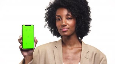 Kendine güveni tam bir kadın kameraya bakıyor, başını sallayarak onaylıyor, elinde yeşil ekranlı bir akıllı telefon tutuyor..