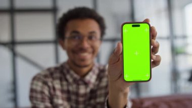 Yeşil ekranlı akıllı telefonu tutan ve cihaza odaklanan gülümseyen bir birey, modeller veya tasarımlar için idealdir.