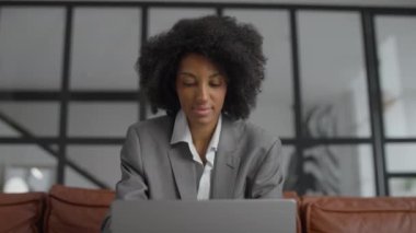 Takım elbiseli profesyonel genç bir kadın, şık ve çağdaş bir ofis ortamında dizüstü bilgisayar kullanırken işine konsantre oluyor..