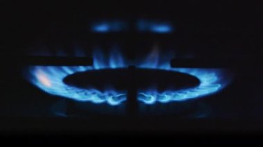 Bir gaz ocağının, koyu bir ortamda parlak mavi alevlerle tutuşmasının detaylı bir görüntüsü..