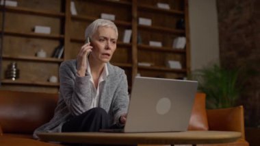 Telefonda üst düzey bir kadın, rahat bir çalışma alanında dizüstü bilgisayar kullanırken destek konularını tartışıyor.