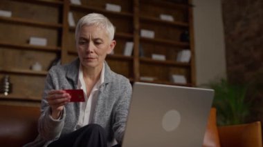 Kredi kartı bilgilerini alışveriş yaparken veya laptopuyla ödeme yaparken girerken odaklanmış yaşlı bir kadın..