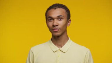 Açık sarı tişörtlü neşeli bir gencin portresi, canlı sarı bir arka plana pozitiflik yayıyor..