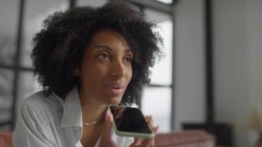 Modern bir iş yerinde odaklanmış profesyonel bir kadın akıllı telefonuna sesli mesaj kaydediyor..