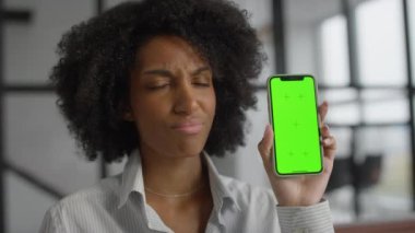 Onaylamadığı için kafasını sallayan bir kadın ofis ortamında yeşil ekranlı bir akıllı telefon tutuyor..