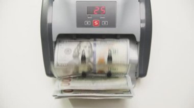 Para sayma makinesi çalışıyor, sayıların dijital ekranda gösterildiği bir yığın ABD doları banknot işleniyor