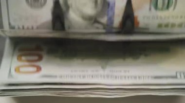 Para sayma makinesinde işlenen bir yığın Amerikan dolarının yakın plan görüntüsü, para birimi ve nakit işleme ekipmanlarının ayrıntılarına odaklanıyor