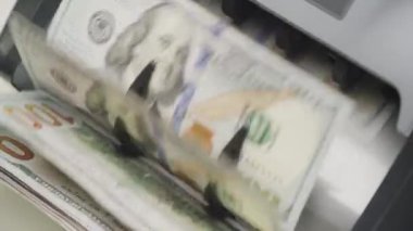 Para sayma makinesinde işlem gören Amerikan dolarlarının yakın plan görüntüleri, nakit işleme hızı ve hassasiyeti vurgulanıyor.