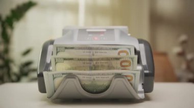 Bir para sayma makinesinin Dolly zoom karesi ve yığınla Amerikan doları banknotları dramatik ve dinamik bir odak yaratıyor..