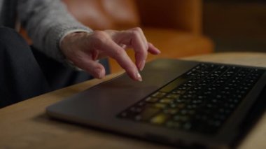 Konforlu bir ortamda internette gezinirken yaşlı bir kadının dizüstü bilgisayara dokunuşunu yakından çek..