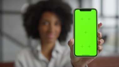 Elinde yeşil ekran ve krom işaretli akıllı bir telefon tutan bir kadın, modern bir ortamda kişiselleştirmeye hazır..