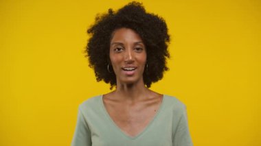 Kıvırcık saçlı ve gülümseyen neşeli bir kadın, canlı sarı bir arka plana kurulmuş bir video görüşmesiyle meşgul..