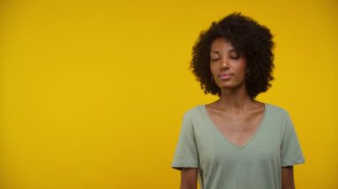 Yeşil gömlekli gülümseyen bir kadın canlı sarı bir arka plana karşı güvenle duruyor, pozitiflik yayıyor, sol tarafında fotokopi alanı var.