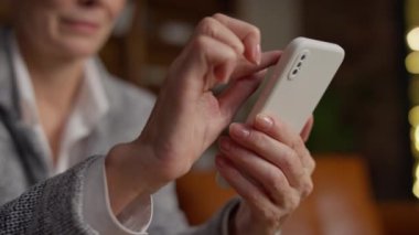 Yaşlı bir kadının elinde akıllı bir telefon tutarken, kapalı mekanlarda dolaşırken slayt ve klik hareketleri yaparken yakın plan çekimleri..