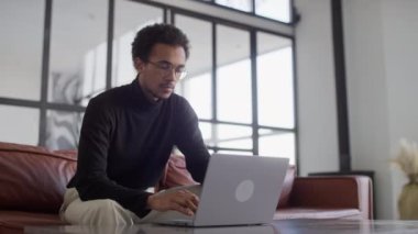 Dizüstü bilgisayarında harika haberler aldıktan sonra koltukta oturan gözlüklü genç adam heyecandan başını tutuyor.