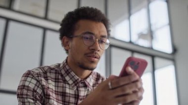 Ekose gömlekli genç adam modern ofis ortamında akıllı telefondan olumsuz bir mesaj okuyor..