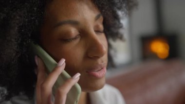 Kapalı mekanda, şöminesi yanan, rahat bir arka planı olan bir kadının telefon konuşması..