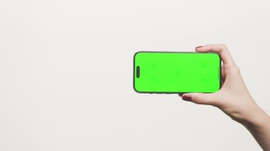 Akıllı telefonu yatay olarak yeşil ekran ile tutan bir el, modeller, uygulama önizlemeleri veya ekran değiştirme projeleri için mükemmeldir.