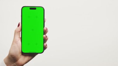 Yeşil ekranlı akıllı telefonu dikey olarak tutan bir elin yakın çekimi, uygulama modelleri, ürün demoları veya tasarımlar için idealdir.