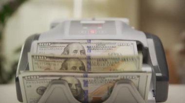 Elektronik para sayma makinesinde işlenen 100 dolarlık banknotların yakın plan görüntüsü, finans ve nakit akışını sembolize ediyor.