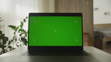 Masasında yeşil ekranlı, doğal ışık ve minimalist dekorla çevrili bir dizüstü bilgisayarın dramatik yakınlaştırma görüntüsü..