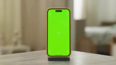Kapalı bir ortamda masanın üzerine yeşil ekran yerleştirilmiş akıllı bir telefonun sinematik zoom görüntüsü..