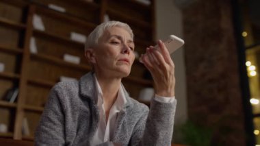 Kendinden emin bir iş kadını sesli mesaj kaydediyor ya da modern bir ofiste akıllı telefonunda ses asistanı kullanıyor..