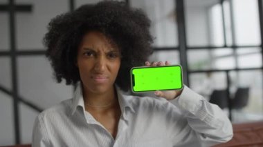Yeşil ekran akıllı telefon tutan profesyonel bir kadın, onaylamadığı halde kafasını sallayarak ofis ortamında memnuniyetsizliğini dile getiriyor..